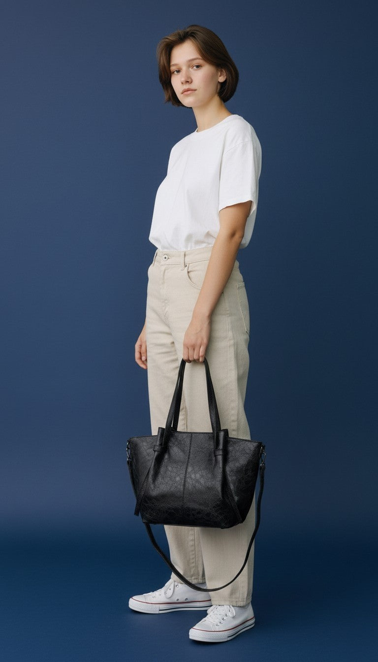 Modella che indossa una borsa tote nera anembags Sara in poliuretano effetto pelle invecchiata su sfondo blu